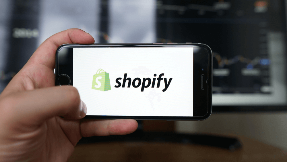 Person holding smartphone displaying Shopify logo